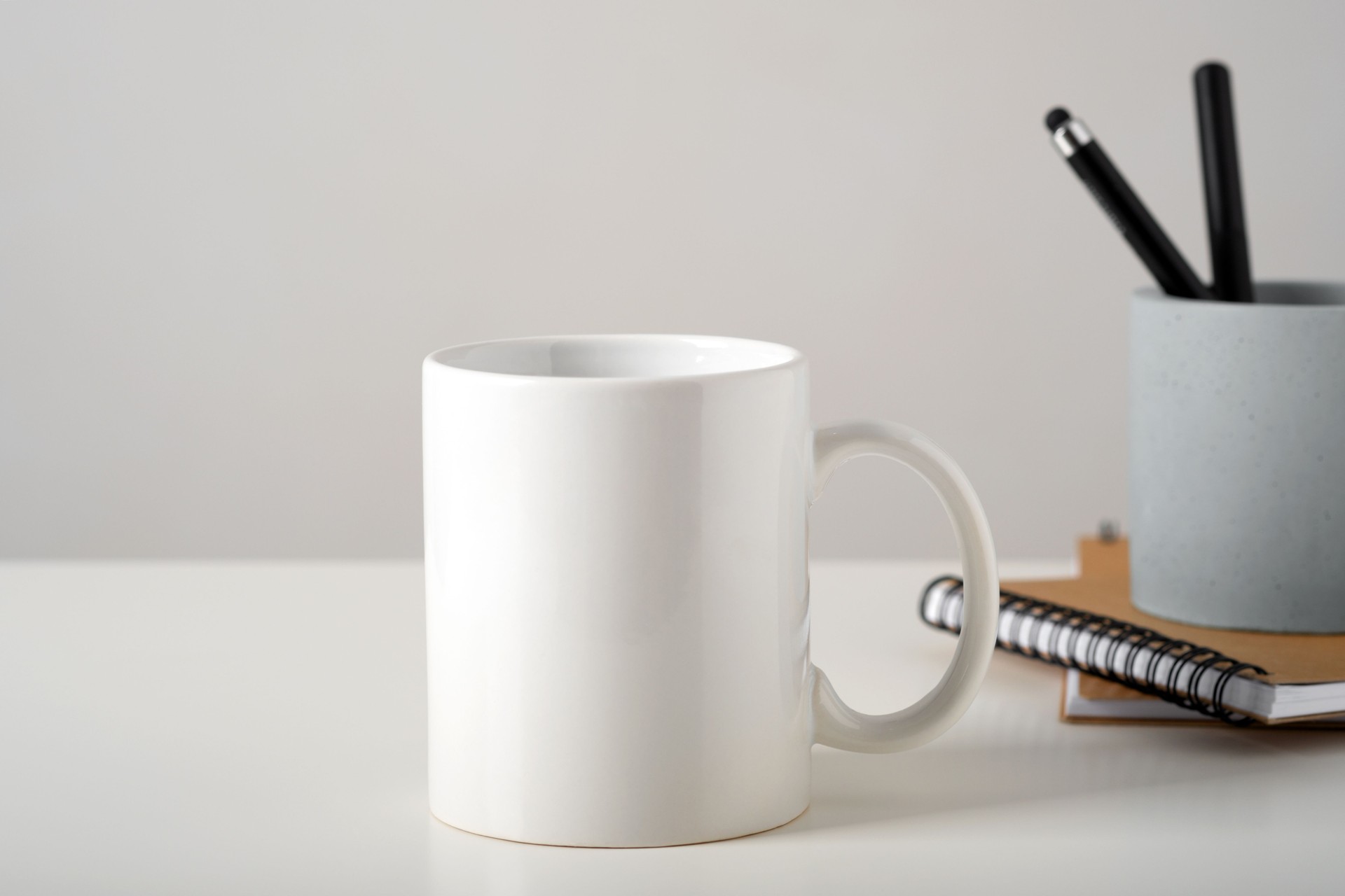 Mockup of a white mug on a table in a minimalist interior, business stationery and notepads. Template, layout for your design, advertising, logo with copy space. Cup on light gray background